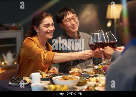 Cheerful woman clinking glasses celebrating Christmas with friends raising toast while sitting together at dining table set with festive dishes Stock Photo