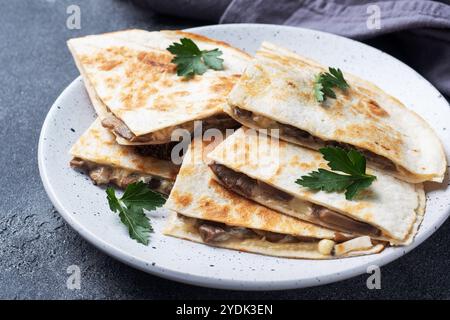 Pieces of quesadilla with mushrooms sour cream and cheese on a plate with parsley leaves. Concrete background close up Stock Photo