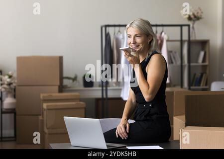 Aged businesswoman working at warehouse using mobile phone voice app Stock Photo