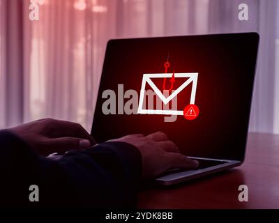 E-mail spam phishing scammer concept. Red warning symbol on envelope in fishing hook icon as bait on laptop screen, criminal hacker cyberattack sendin Stock Photo