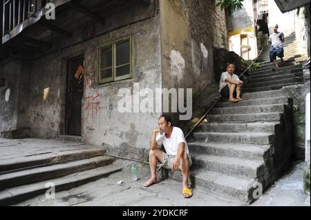 04.08.2012, Chongqing, China, Asia, Men sit on the steps in front of an old house in the old town of Shibati, on whose wall red letters inform the res Stock Photo