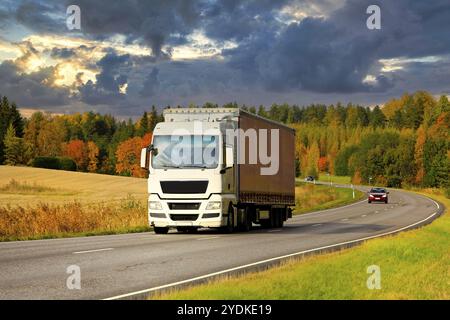 White semi trailer truck on highway at speed transporting goods on a beautiful autumn evening Stock Photo