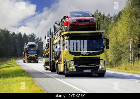 Two vehicle carriers, yellow Volvo FM truck in the front, haul new cars on road 52 from Hanko Port to mainland. Raasepori, Finland. September 9, 2021 Stock Photo