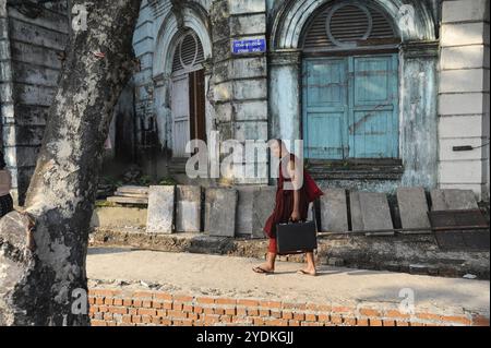 07.10.2013, Yangon, Myanmar, Asia, A Buddhist monk walks with his briefcase past an old colonial building on the famous Strand Road, Asia Stock Photo