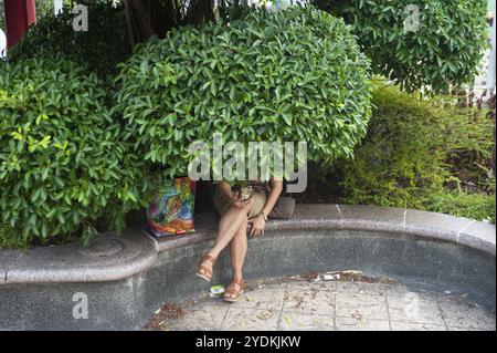 24/02/2019, Singapore, Republic of Singapore, Asia, A woman sits under a tree in the garden of the People's Park Complex in Singapore's Chinatown dist Stock Photo