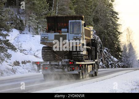 Black Volvo FMX truck Lonnqvist Oy hauls Hitachi CG 110 tracked dumper on flatbed trailer on highway 52 in winter. Salo, Finland. December 28, 2021 Stock Photo