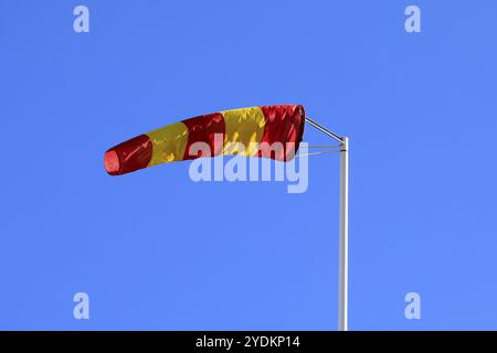 Yellow and red striped windsock or wind cone against clear blue sky, indicating wind direction and force. Copy space for your text Stock Photo