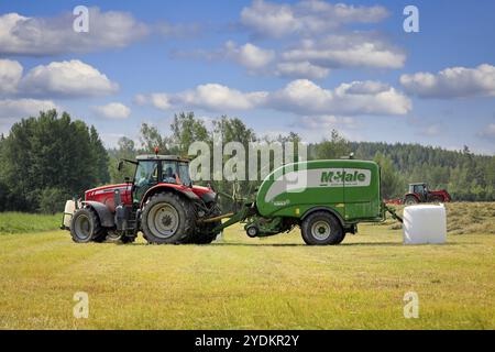 Massey-Ferguson tractor in hay field with McHale baler wrapper harvesting dry hay in the summer. Raasepori, Finland. June 25, 2021 Stock Photo