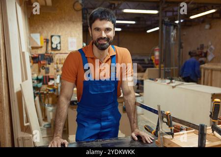 Portrait of smiling craftsman in coveralls at workplace in carpentry shop Stock Photo