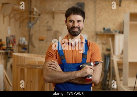 Portrait of smiling man carpenter in coveralls holding drill power tool Stock Photo