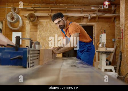 Man professional carpenter wearing workwear working with wood plank Stock Photo