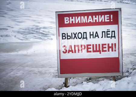 People walking near a sign warning: prohibited walking on thin ice, winter landscape with frozen lake Stock Photo