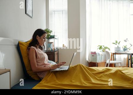 Young Woman Typing on Laptop in Cozy Bedroom Stock Photo