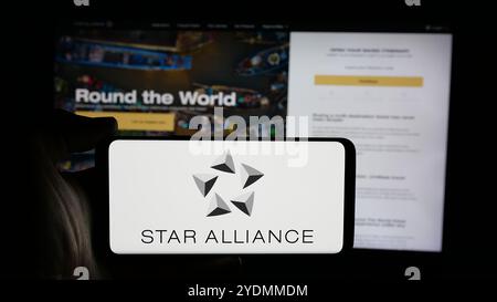 Person holding cellphone with logo of airline organisation Star Alliance on screen in front of webpage. Focus on phone display. Stock Photo