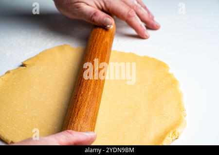 Men's hands roll out shortcrust dough with a rolling pin on a white table. The baker is working with the dough. Recipe for making a pie or cookies. Hi Stock Photo