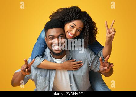 Cheerful black lady piggybacking her boyfriend and showing peace sign Stock Photo