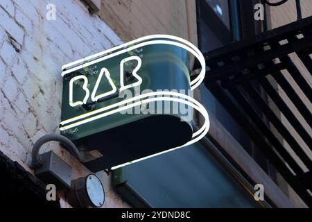 Neon bar sign with geometric art deco logo mounted on a textured brick wall in an urban setting manhattan nyc usa Stock Photo
