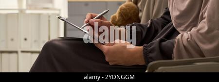 Person using stylus on tablet in modern office environment, focusing on technology for note-taking. Background shows shelves with organized binders Stock Photo