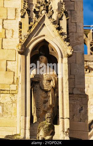 A close-up of a stone statue in a niche on the side of a building. The statue is of a man with a beard and long robes, holding a book. The niche is de Stock Photo