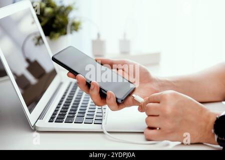 Man charging smart phone in the office, using charger Stock Photo