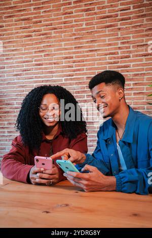 Vertical African American couple using their cellphones at home, smiling and sharing moments together, Two friends enjoying technology and connectivity in a cozy, modern living space with brick wall. High quality photo Stock Photo