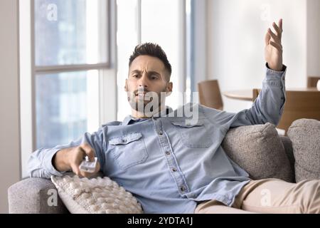 Nervous Latin man using TV remote control on home couch Stock Photo