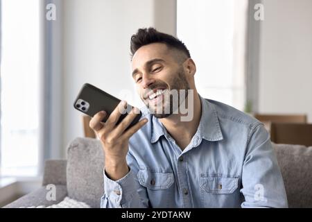 Happy handsome Hispanic man using voice assistant on mobile phone Stock Photo