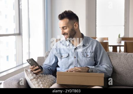 Happy young Hispanic customer guy holding smartphone and logistic box Stock Photo