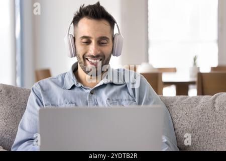 Positive handsome Hispanic man in wireless headphones using laptop Stock Photo