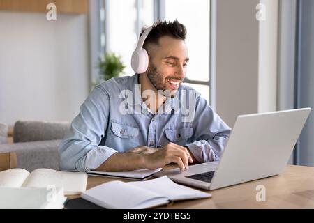 Happy Latin student man in headphones studying online at laptop Stock Photo