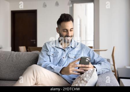 Cheerful young Latin man typing on mobile phone Stock Photo