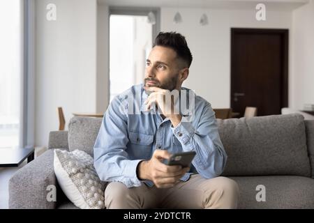 Thoughtful dreamy Hispanic man holding mobile phone and looking away Stock Photo