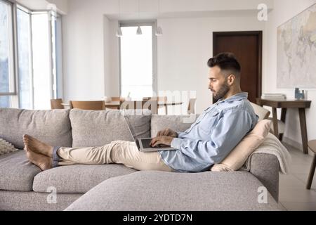 Focused relaxed young Hispanic man resting on comfortable sofa Stock Photo
