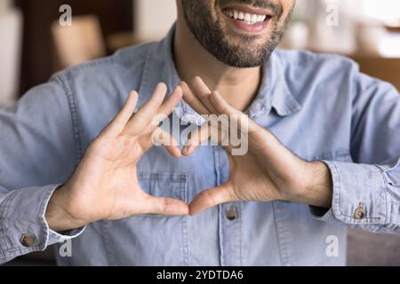 Cheerful young Caucasian man keeping hand heart gesture at chest Stock Photo
