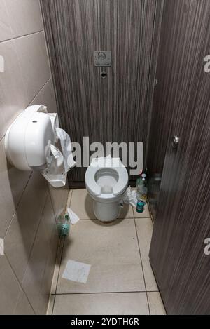 Toilet cubical in Liverpool Street station with empty alcohol and water bottles and cans on the floor, with paper and damaged toilet roll dispensers Stock Photo