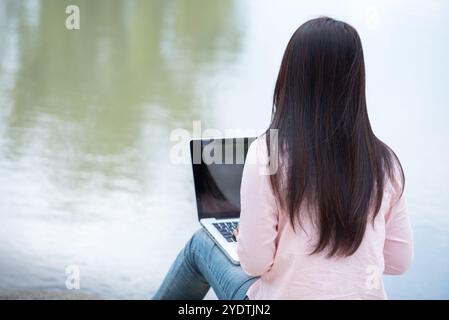 Asian woman sitting green park using laptop computer. Woman working on laptop happy entrepreneur business using notebook with hands typing on keyboard Stock Photo