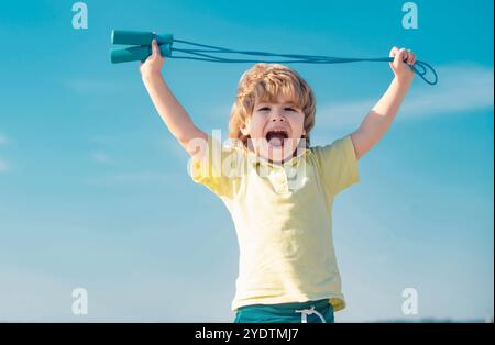 Portrait of cute boy exercising with jumping rope on blue sky background. Kid skipping rope during sunny morning. Stock Photo