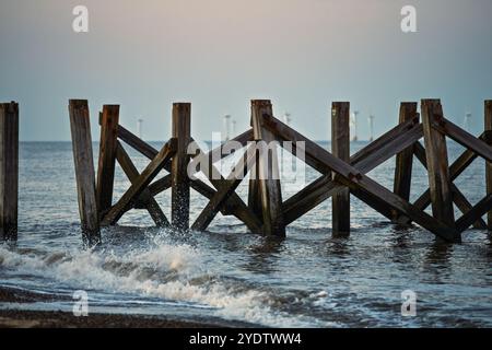 Sunset over the pier on the beach with wind farm on the background. Stock Photo
