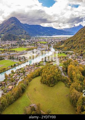 Aerial view of a village surrounded by green fields and mountains, river in the foreground, cloudy sky, Interlaken, Switzerland, Europe Stock Photo