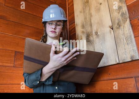 Construction female inspector using a clipboard to taking notes. a young caucasian woman worker wearing hard hat at work, low angle portrait Stock Photo