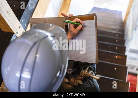 Top view of construction inspector woman sits on the stairs during a home pre-purchase inspection, she uses clipboard to writes notes. with copy space Stock Photo
