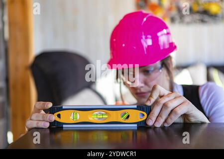 Close up and selective focus shot of spirit level tool used by a female architect, she wearing a pink hardhat and protective eyewear in the background Stock Photo