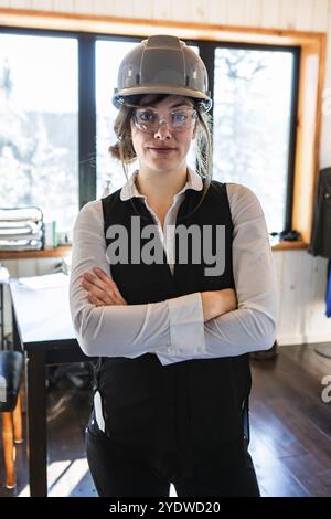 Young attractive caucasian woman with crossed arms pose as she wearing classy work clothes with safety grey hard hat and protective eyewear glasses Stock Photo