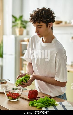 A handsome young man skillfully mixes fresh ingredients for a colorful salad in his elegant kitchen. Stock Photo