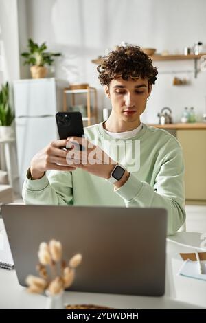 A handsome young man is engaged in remote work at his modern apartment, focused on his smartphone. Stock Photo