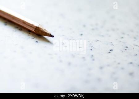 This is a detailed close up view of a pencil resting gently on a white piece of paper, highlighting the texture and color of both items Stock Photo