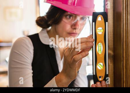 Attractive female construction inspector wearing protective eyewear and pink hard hat as she using a spirit level. Home inspection and quality control Stock Photo