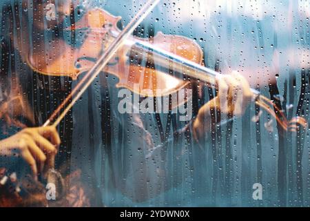Playing violin song behind the window with water drops on a rainy day. Sad music for travel road.Violin and clasical music concept abstract background Stock Photo