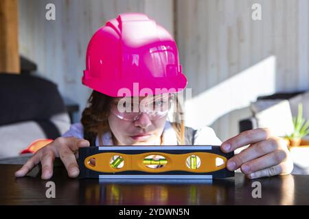 Young caucasian woman architect wearing a pink hard hat and protective eyewear, she measuring horizontal surface with a spirit bubble level tool Stock Photo