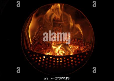 Logs burn and glow in a wood-burning stove with a round glass window Stock Photo